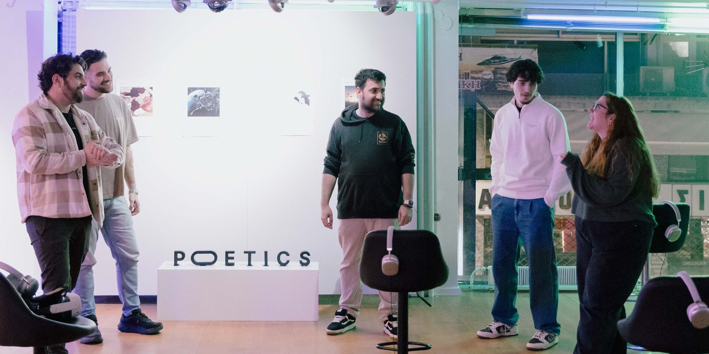 Five people talking and laughing in the Poetics pop-up at Toss Gallery, beside the Poetics sign and stools with headsets.