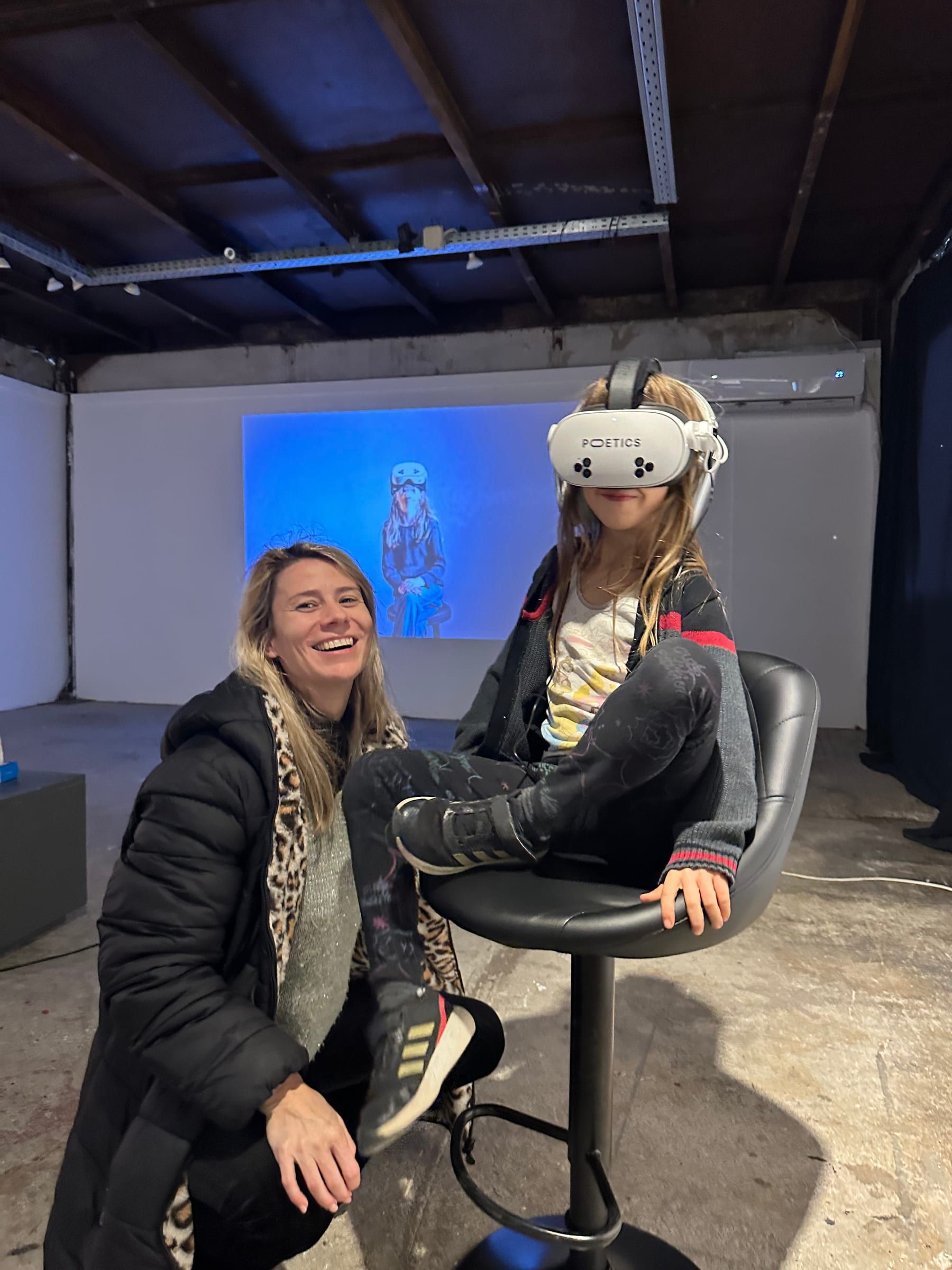 A child in a headset on a stool, with an adult kneeling beside them, smiling.