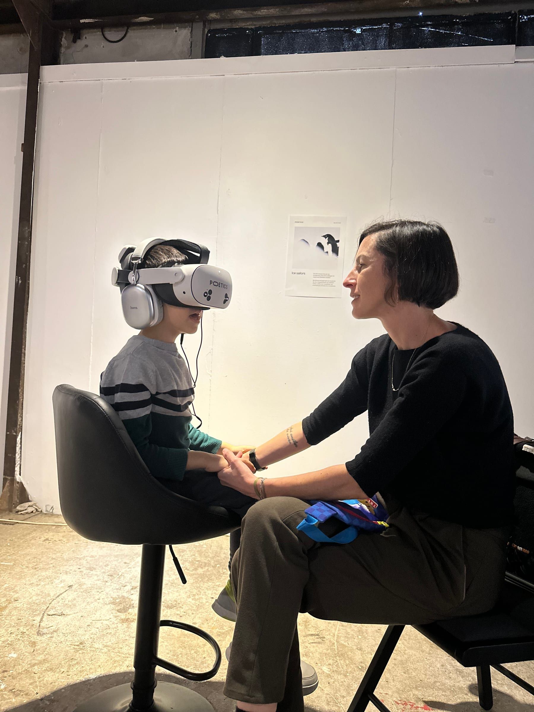 A child in a headset and an adult seated beside them, holding their hands.