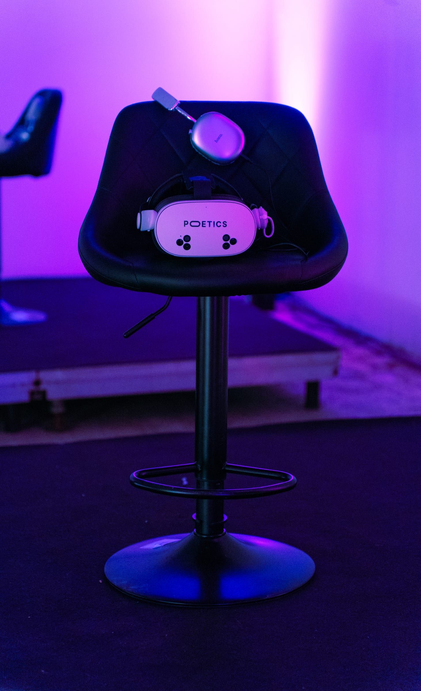 A black Poetics stool with a headset resting on it, in purple light.