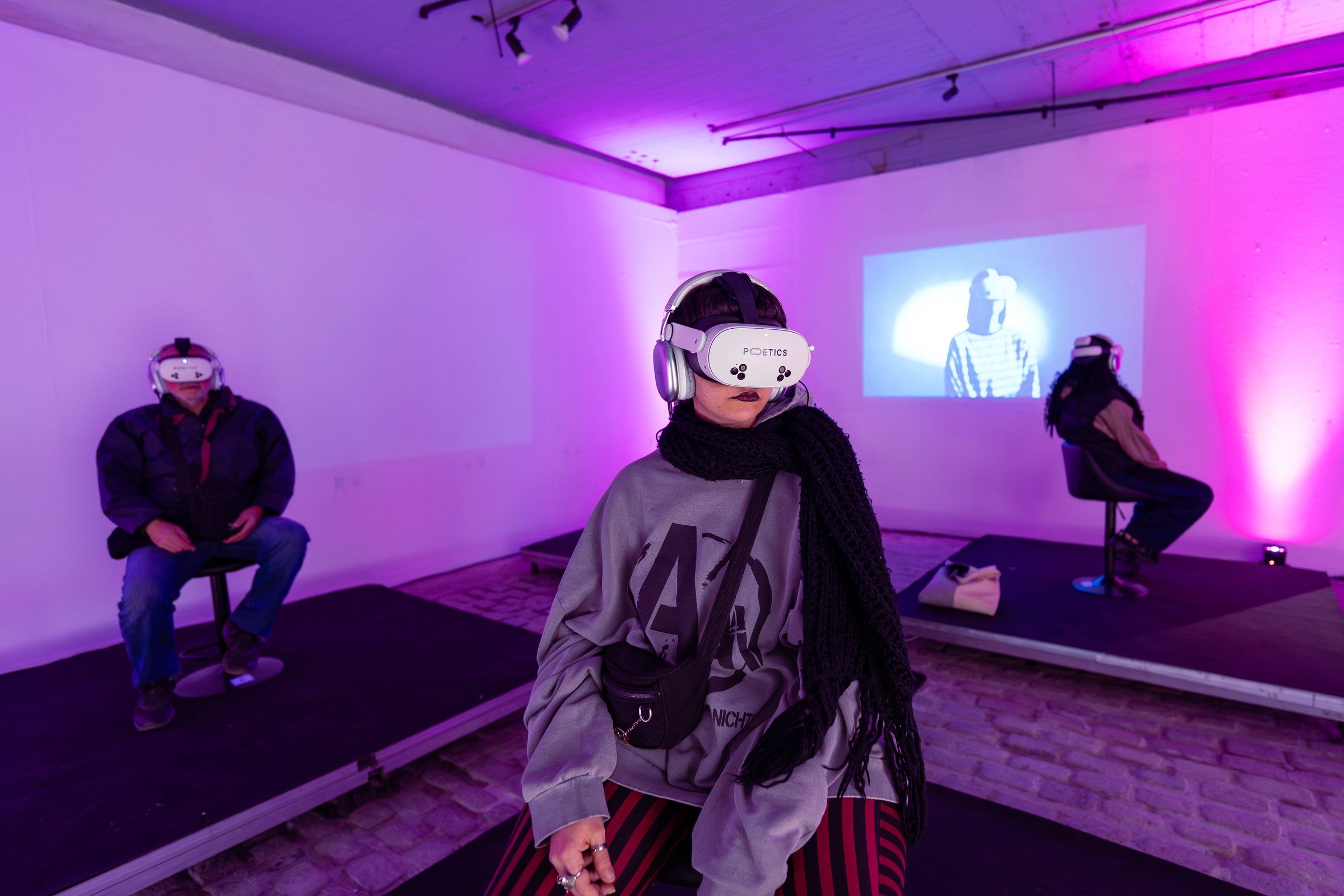Three visitors in headsets on low platforms in a purple-lit room, with a film on the far wall.