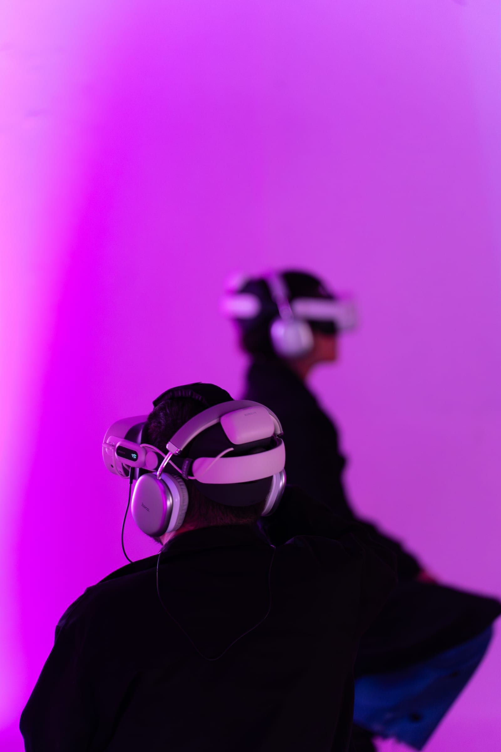 Two visitors in headsets against a magenta wall.