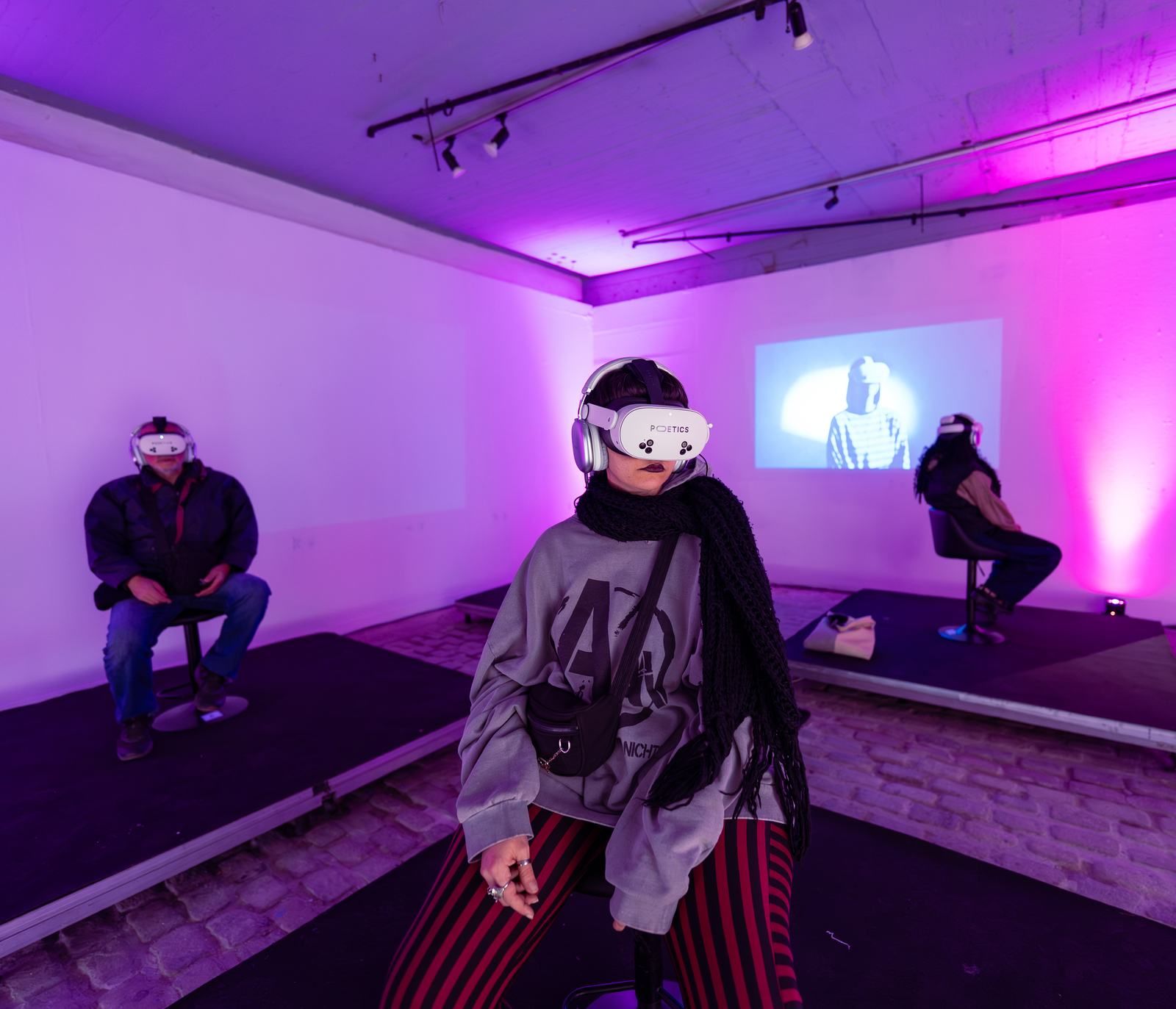 Three Poetics VR stations in a purple-lit room.
