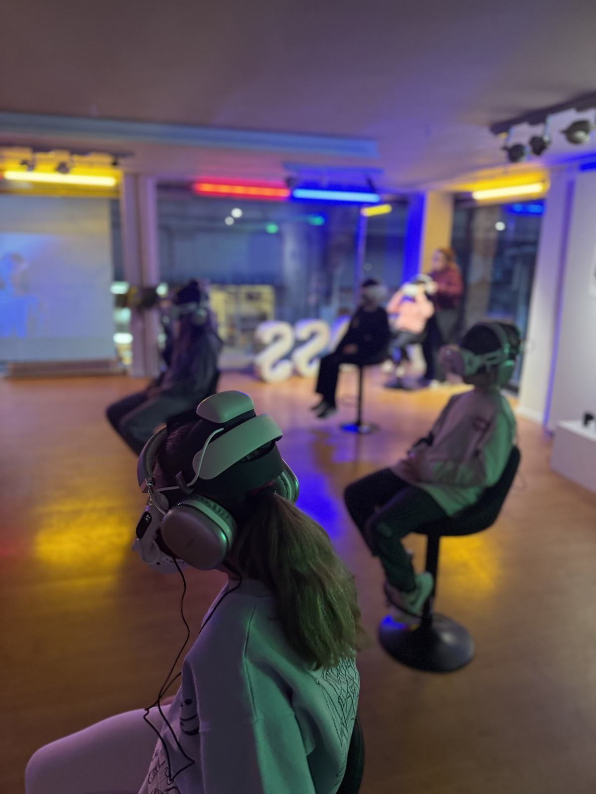 Visitors watching VR in a colorful room of several stations.