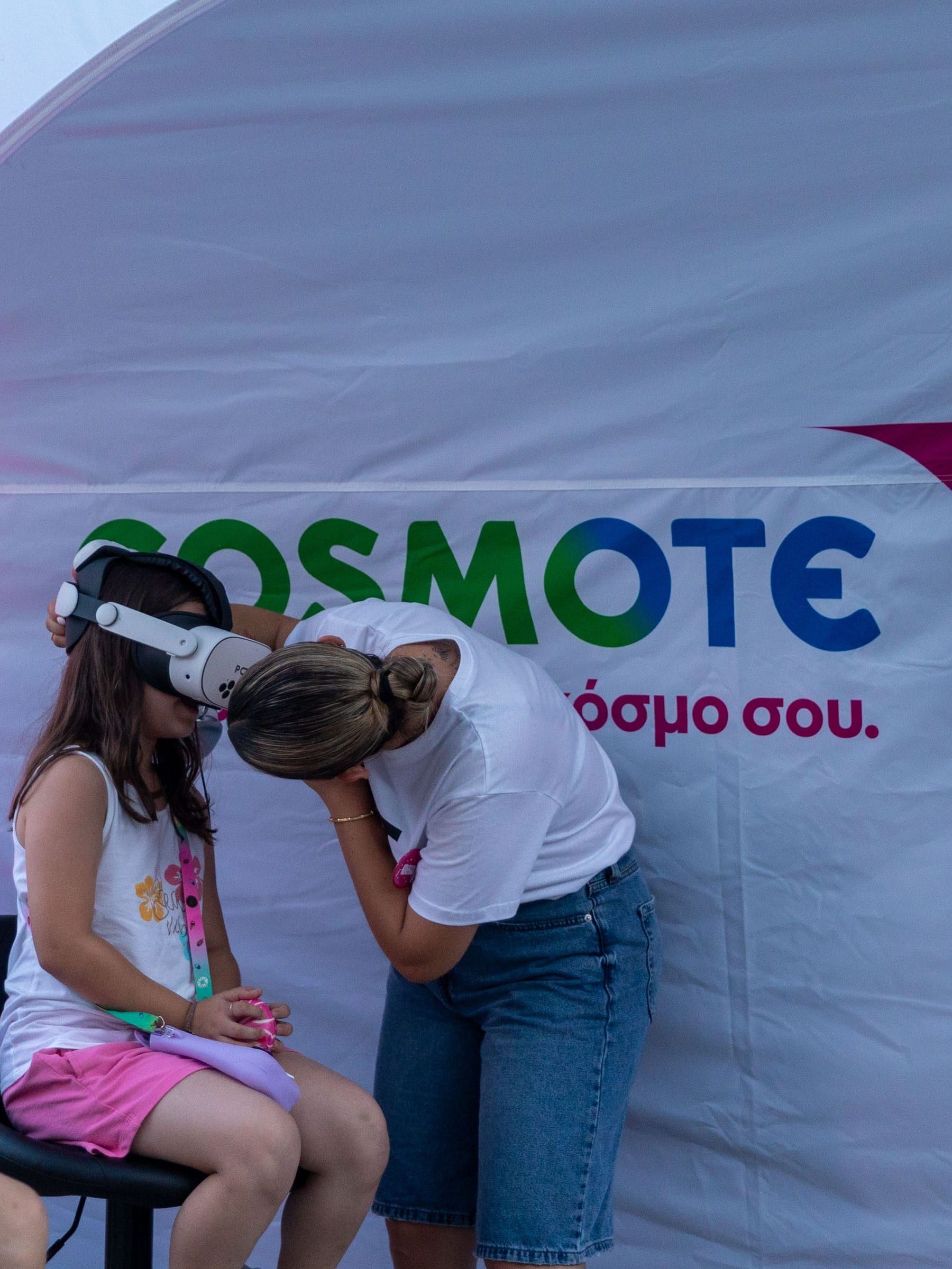 A child in a headset and a staff member leaning toward each other in front of the tent wall.