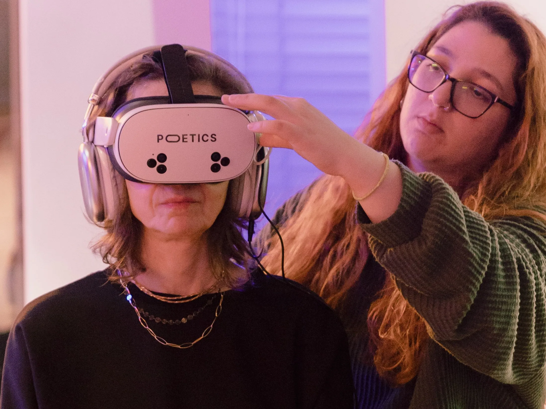 An operator adjusts a Poetics headset on a seated visitor wearing headphones.