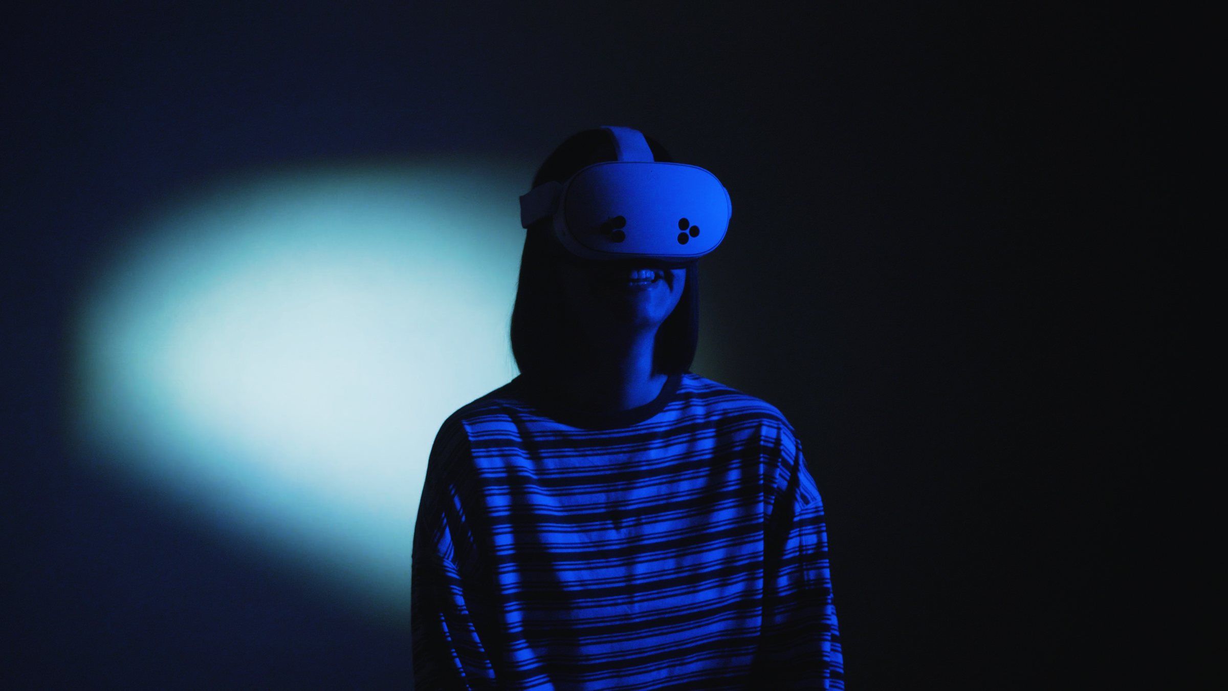 A visitor in a striped top wears a headset in the dark, lit by a pool of blue light.