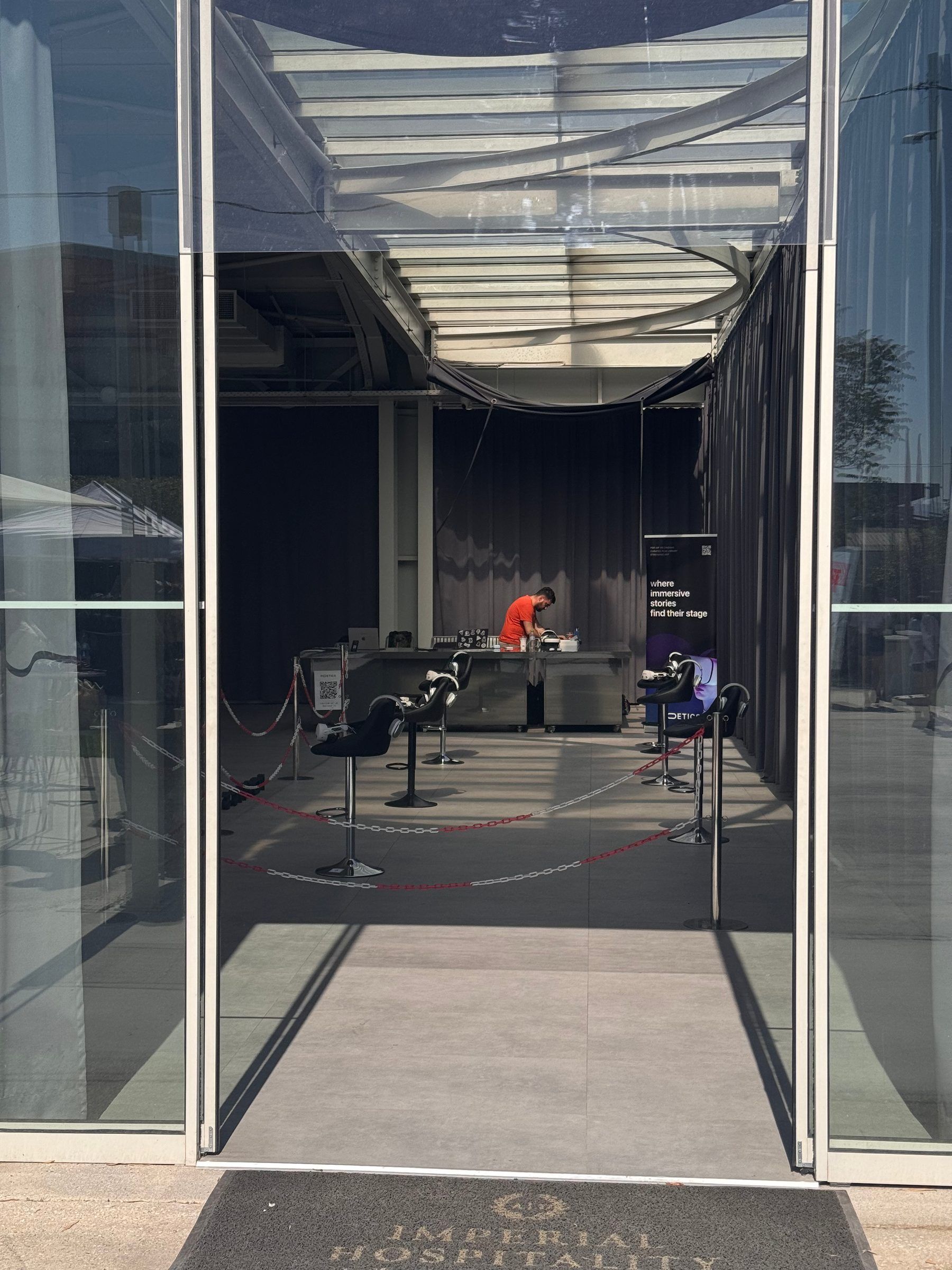 The view through the glass entrance, with the empty stools roped off and an operator preparing headsets at the desk.