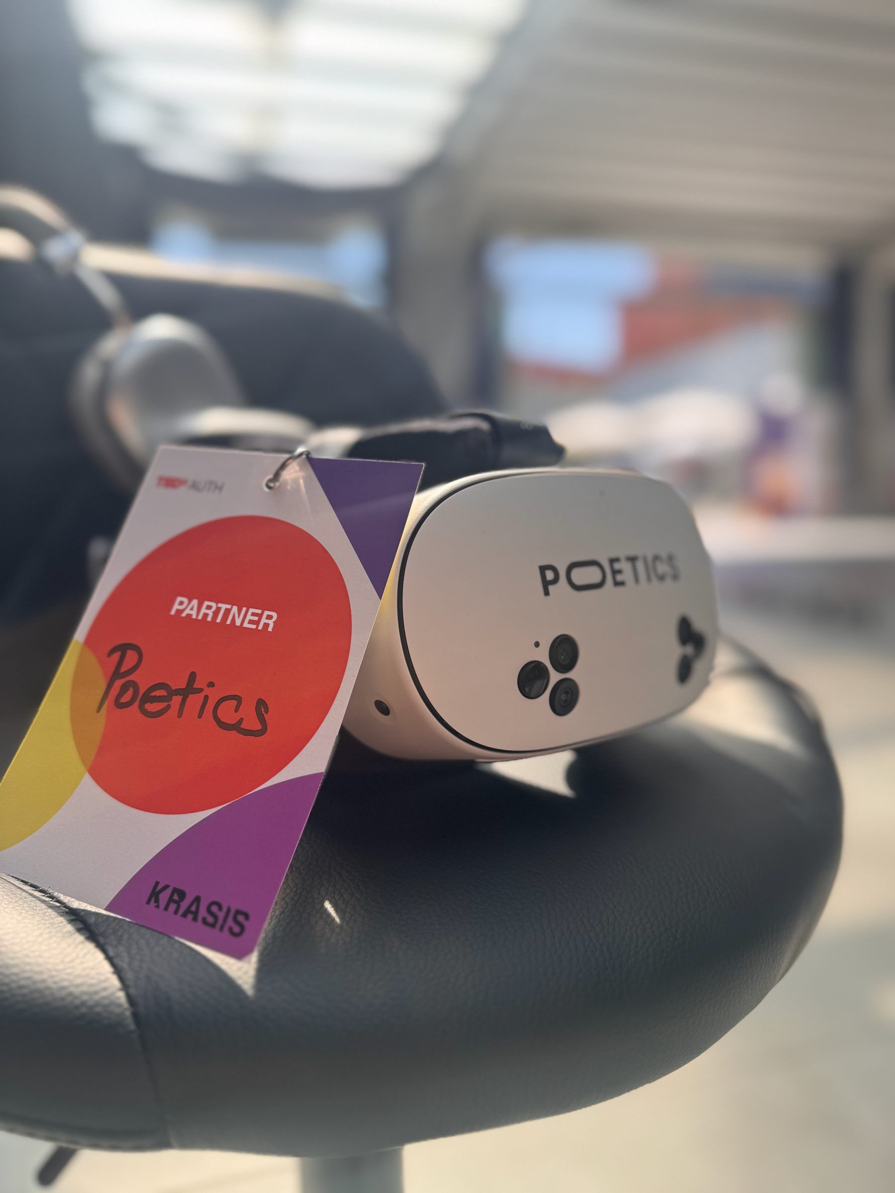 A Poetics headset on a stool, with a TEDxAUTH partner badge reading Poetics hung beside it.