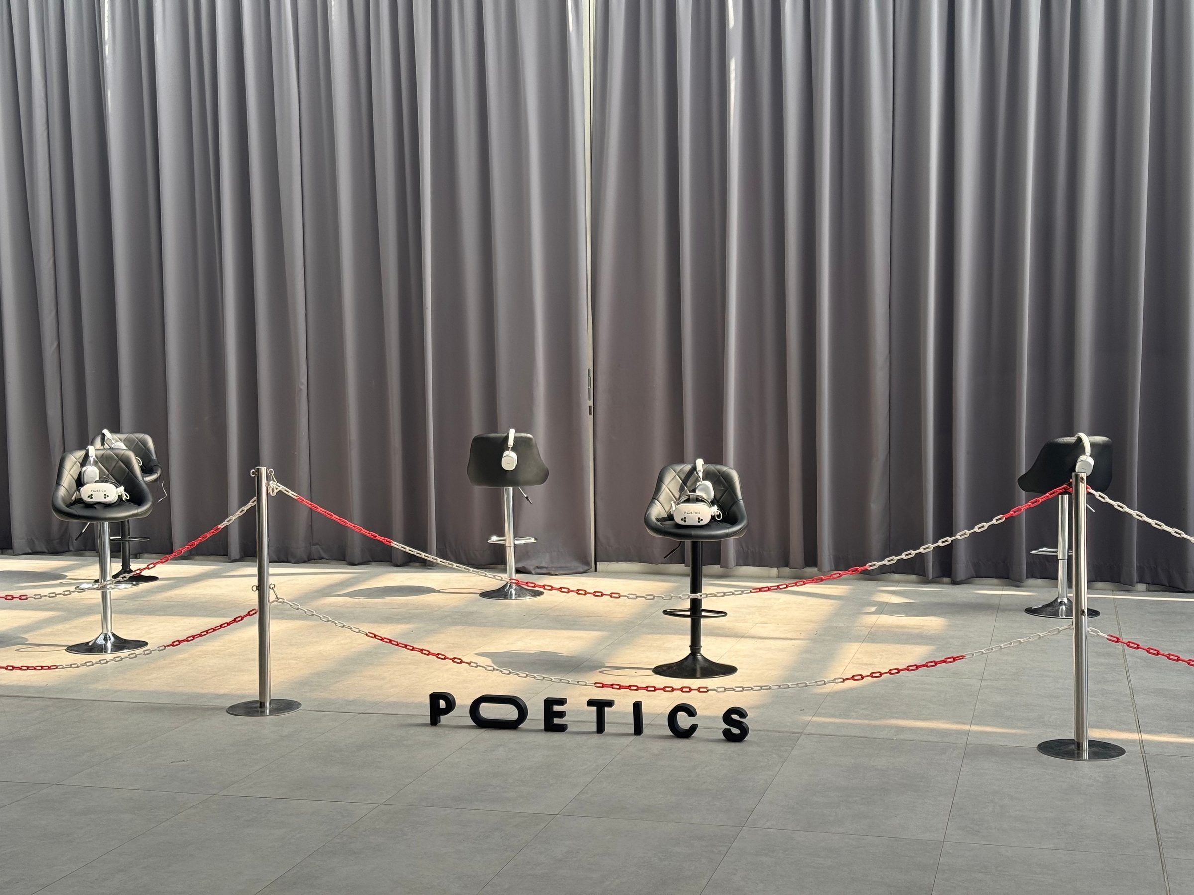 Empty stools with headsets and headphones on their seats, behind a rope line, with the Poetics letters standing on the floor.