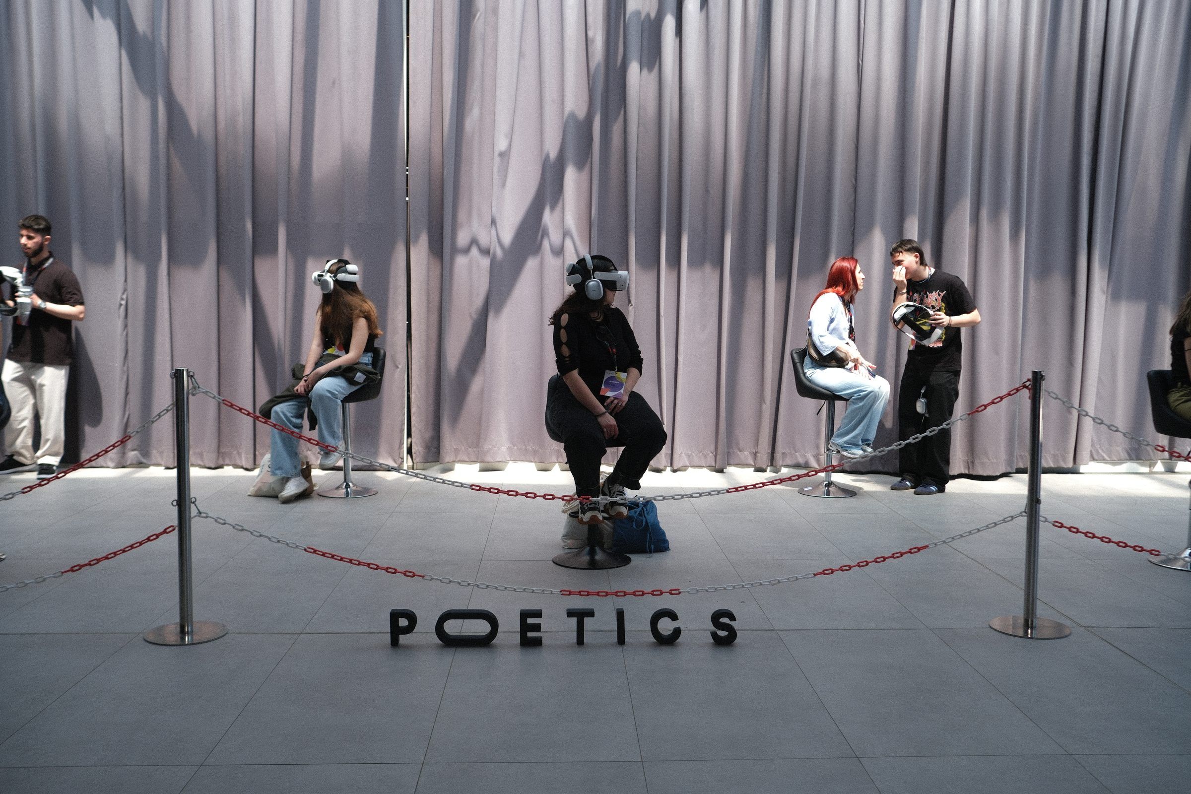 Viewers in headsets on stools behind a rope line, an operator talking with a visitor, and the Poetics letters on the floor in front.